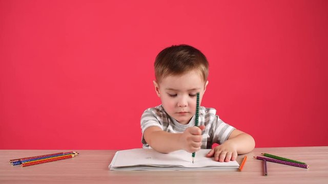 Happy child drawing with pencils in album, isolated on pink.