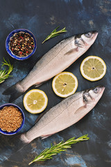 Two raw sea bass fish with spices, lemon and rosemary on a blue abstract background. View from above.