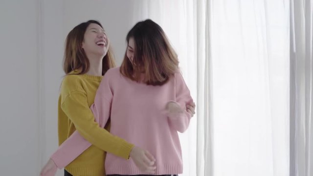 Beautiful young asian women LGBT lesbian happy couple or Girls Friends dancing to streaming music having wild fun in pajamas on bed in teenage bedroom hanging out at home. Spending nice time at home.