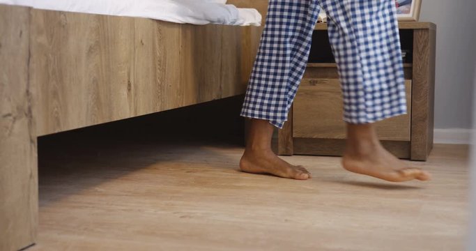 Close up of the woman's barefeet jumping out the bed on the floor early in the morning and walking to the window. Inside