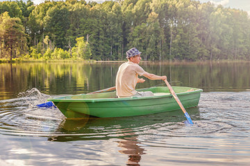 Fisherman with fishing rods is fishing in a wooden boat against background of beautiful nature and lake or river. Camping tourism relax trip active lifestyle adventure concept