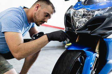 Fototapeta na wymiar Motorcycle detailing - Man with orbital polisher in repair shop polishing motorcycle. Selective focus.