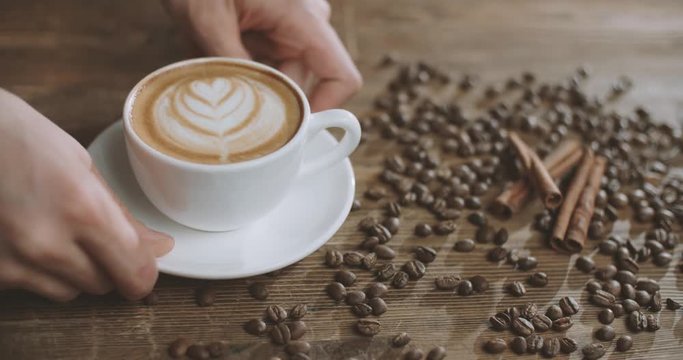 the beautiful composition of the Barista puts a cappuccino on the table with coffee beans and cinnamon