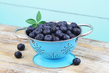 Fresh blueberries in blue colander on rustic wooden surface
