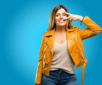 Beautiful young woman looking at camera through her fingers, blue background