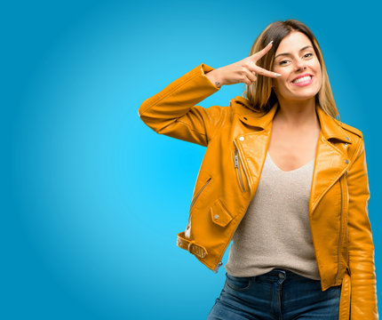 Beautiful young woman looking at camera through her fingers, blue background