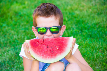 Child eating juicy watermelon outdoors on grass