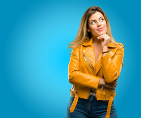 Beautiful young woman thinking and looking up expressing doubt and wonder, blue background