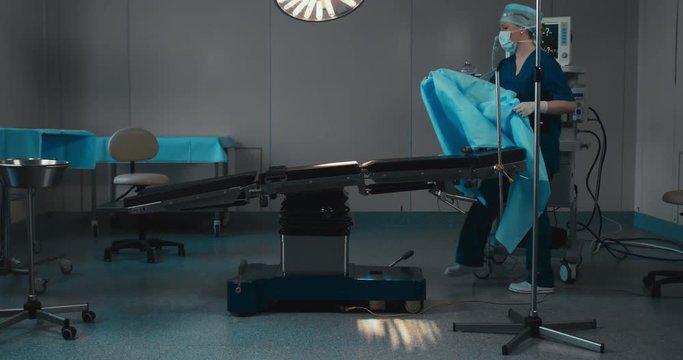 DOLLY IN WIDE female nurse covering table with sterile tissue, preparing operating theatre for operation. 4K UHD 60 FPS SLO MO