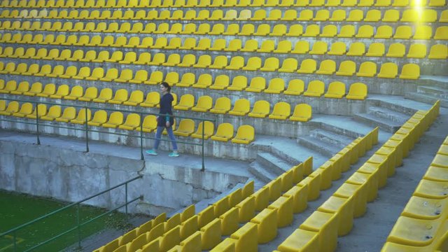 The girl in the blue windbreaker is leaving the podium of the stadium. Canceled match, game. An empty stadium without fans. Spectators are not allowed into the stadium. 4k
