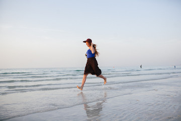 Fototapeta na wymiar A beautiful girl runs along the shore of the sea against a beautiful sunset