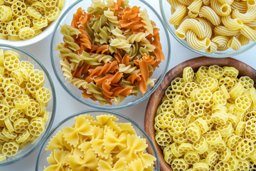 Macaroni ruote Different pasta in a glass and wooden bowl with pasta spirals on a white background, close-up view from the top.