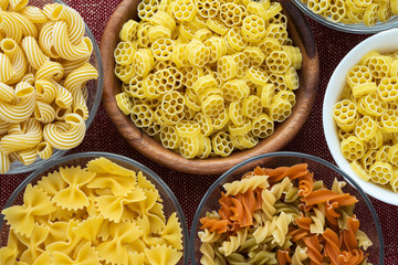 Macaroni ruote Wooden white and glass bowl with various pasta spirals on a textured red brown background, close-up view from the top.