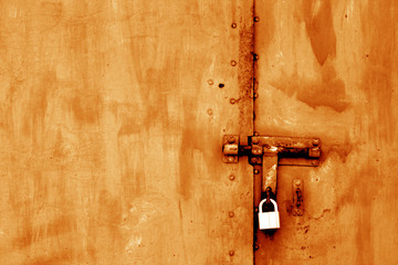 Old padlock on metal gate in orange tone.