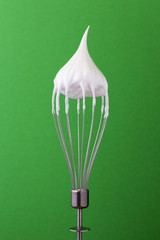 Metal whisk with whipped egg whites on green background