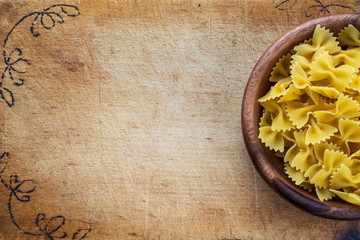 farfalle macaroni pasta in a wooden bowl on a cutting wooden board, texture background with a side. Close-up with the top. Free space for text.