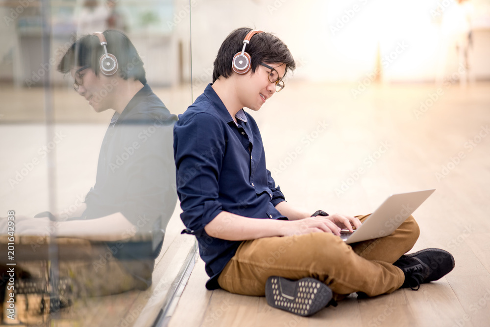 Wall mural reflection of young asian business man enjoy listening to music by headphones while using laptop com