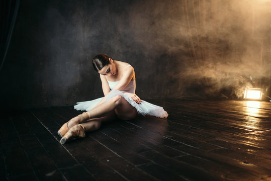 Ballerina in white dress sitting on stage