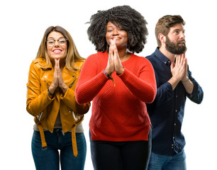 Group of three young men and women with hands together in praying gesture, expressing hope and please concept