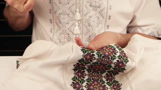 Man in ukrainian national shirt embroiders on white linen