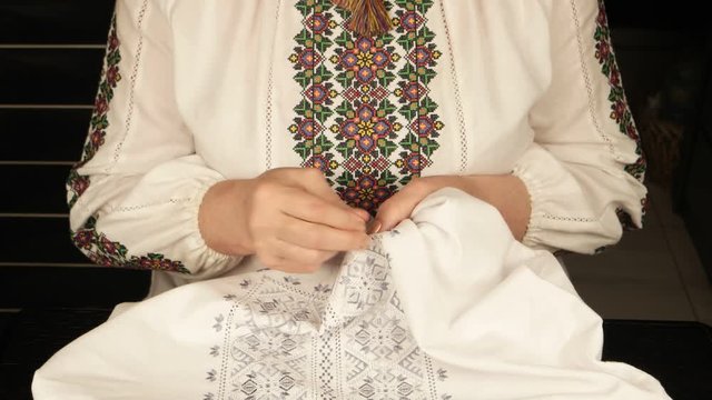 Woman in ukrainian national shirt embroiders on white linen

