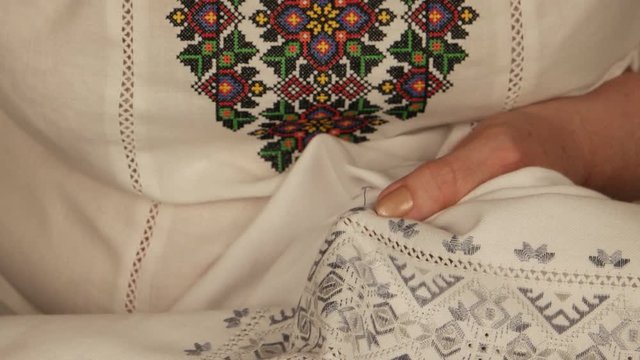Woman in ukrainian national shirt embroiders on white linen

