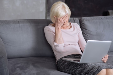 Elderly busy woman working on laptop and having headache.