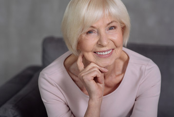 Happy mature lady keeping hand near head and smiling.