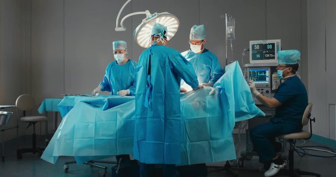 Medical team, doctors performing surgical operation in real modern operating theater. 4K UHD 60 FPS SLO MO