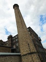 old industrial stone mill building with tall chimney in huddersfield west yorkshire