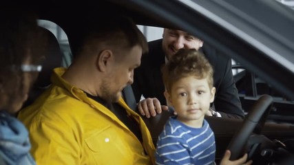 Content multiracial couple with son sitting in car and talking with dealer in auto shop giving credit card for payment to manager. - Powered by Adobe