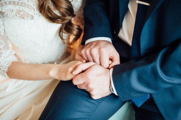 Naklejka premium Close-up of the groom's hands in a blue suit holding the bride's hands in a white wedding dress, horizontal