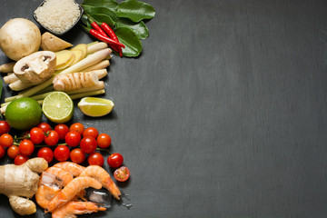 Special ingredients for popular Thai spicy soup Tom-yum kung lime, galangal, red chili, cherry tomato, lemongrass and kaffir lime leaf on black table with copy space. View from above.