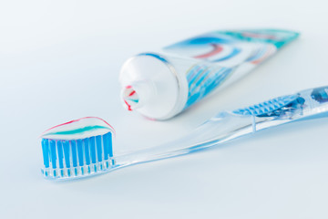 toothbrush of clear plastic with blue bristles, white blue red toothpaste squeezes out of a tube