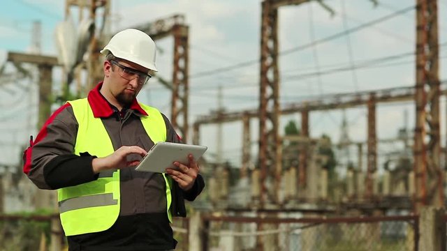 Worker in hard hat at electric power plant, engineering supervision. Electrician with computer on power station. Factory worker with tablet pc