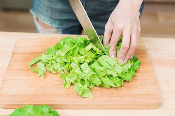 Close-up Female hands chopping a green plant salad cooking salad from vegetables on a wooden cutting board at home. The concept of vegetarianism and healthy lifestyles