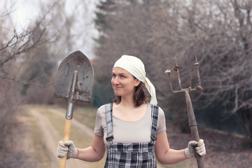 Gardener/farmer woman with spade and pitchfork on the rural road.