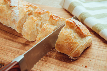 Fresh sliced baguette with knife on a cutting board