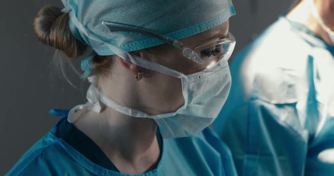 EXTREME CU Portrait of nurse assisting in surgical operation in real modern operating theater. 4K UHD 60 FPS SLO MO