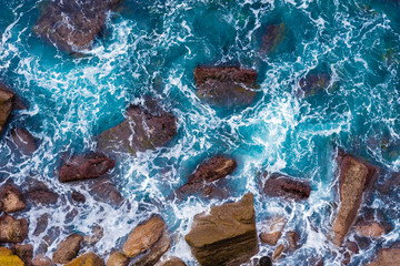 Top aerial view of blue waves crashing on rocky Australian coastline. Summer seascape with ocean waves and cliffs. Travel concept background