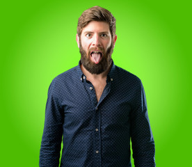 Obraz premium Young hipster man with big beard feeling disgusted with tongue out over green background