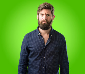 Young hipster man with big beard making funny face fooling over green background