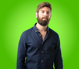 Young hipster man with big beard making funny face fooling over green background