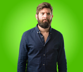Young hipster man with big beard making funny face fooling over green background