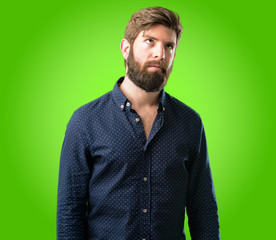 Young hipster man with big beard making funny face fooling over green background