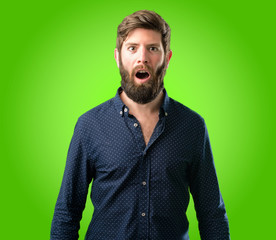 Young hipster man with big beard scared and surprised cheering expressing wow gesture. Unbelieving over green background