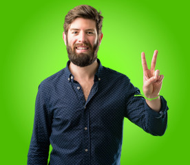 Naklejka premium Young hipster man with big beard raising his fingers, number two over green background