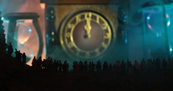 Silhouette of a large crowd of people in forest at night standing against a big arrow clock with toned light beams on foggy background. Time concept. Hourglass measuring the passing time