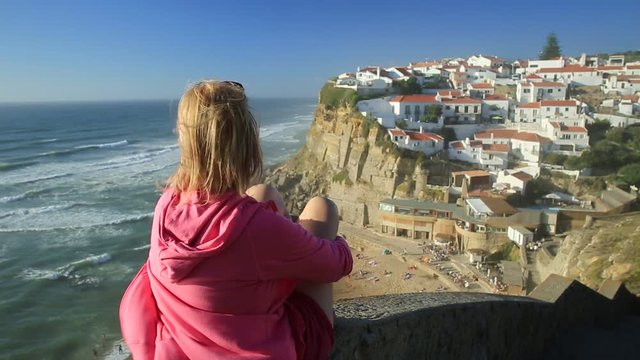 Happy sporty woman looking Azenhas do Mar on the Atlantic Ocean. backside tourist girl at Portuguese seaside resort near Colares. Tourism and travel in Portugal.
