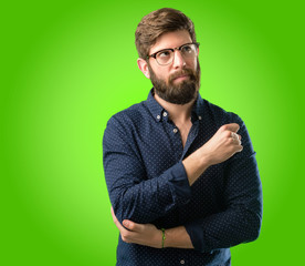 Young hipster man with big beard pointing away side with his finger over green background